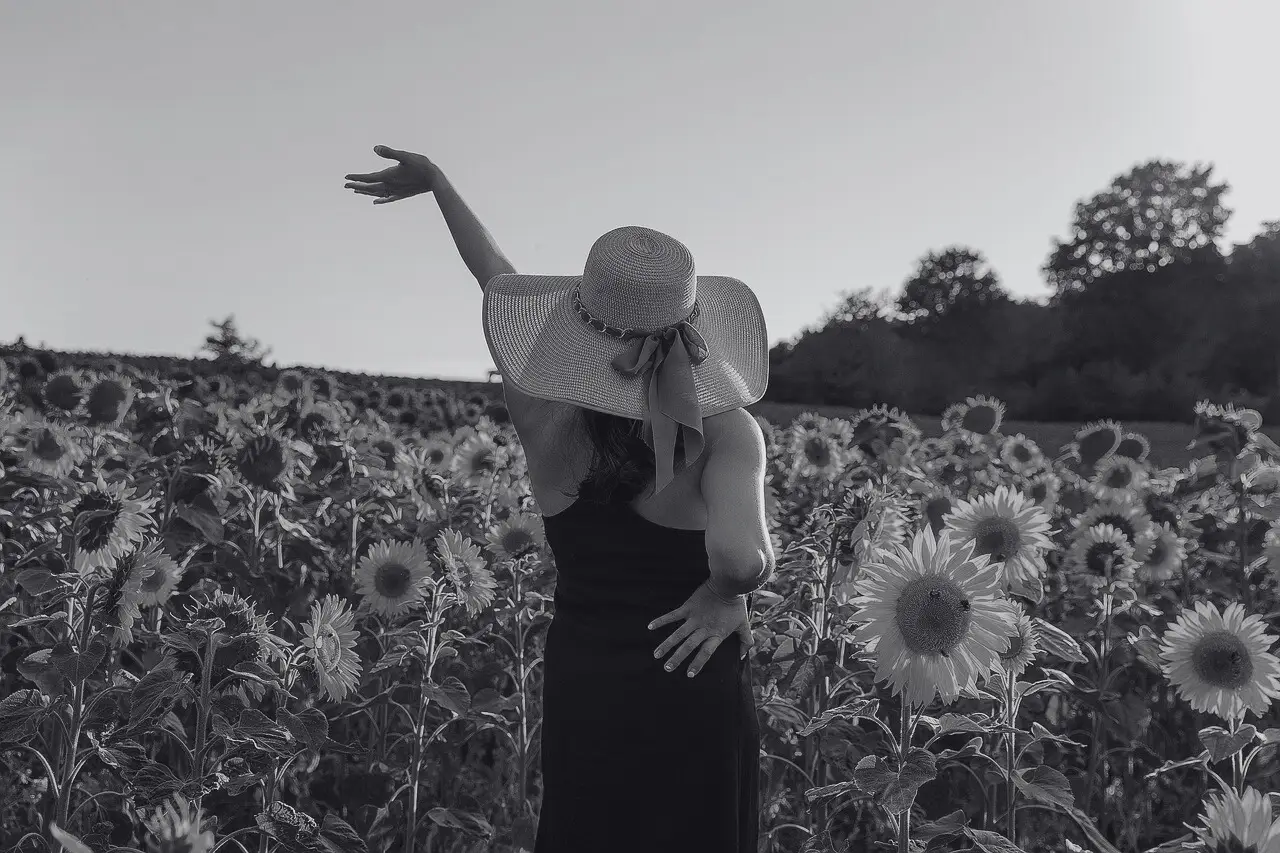 Frau mit Strohhut und dunklem Kleid im Sonnenblumenfeld, Arm erhoben, Symbolbild zum Thema Poland Syndrom bei BONITAS in Nürnberg