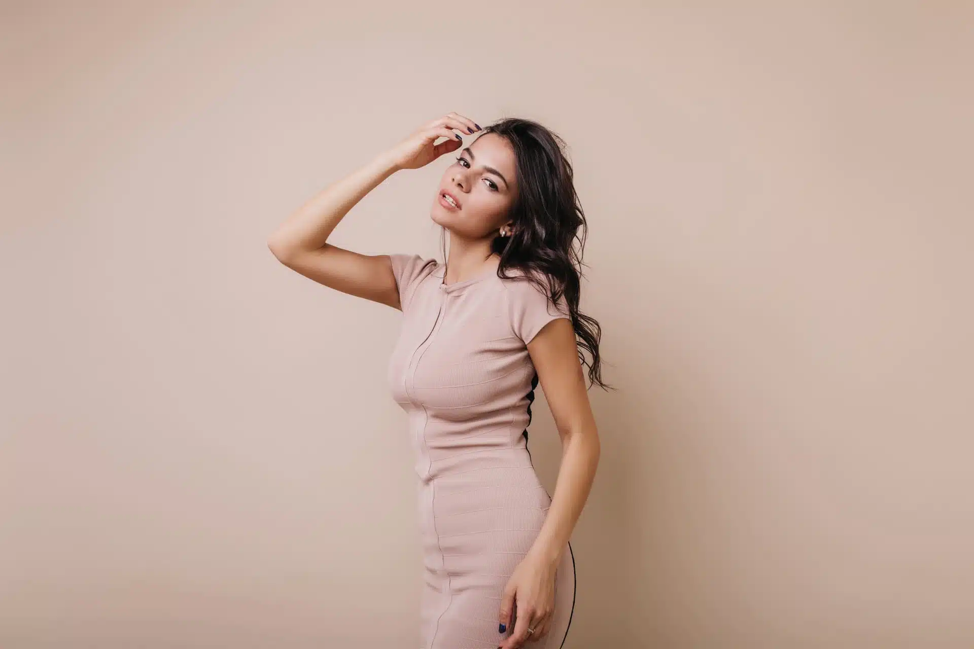 Mujer en vestido claro posa con mano en la frente ante pared beige, imagen simbólica sobre Aumento de mentón en BONITAS Núremberg