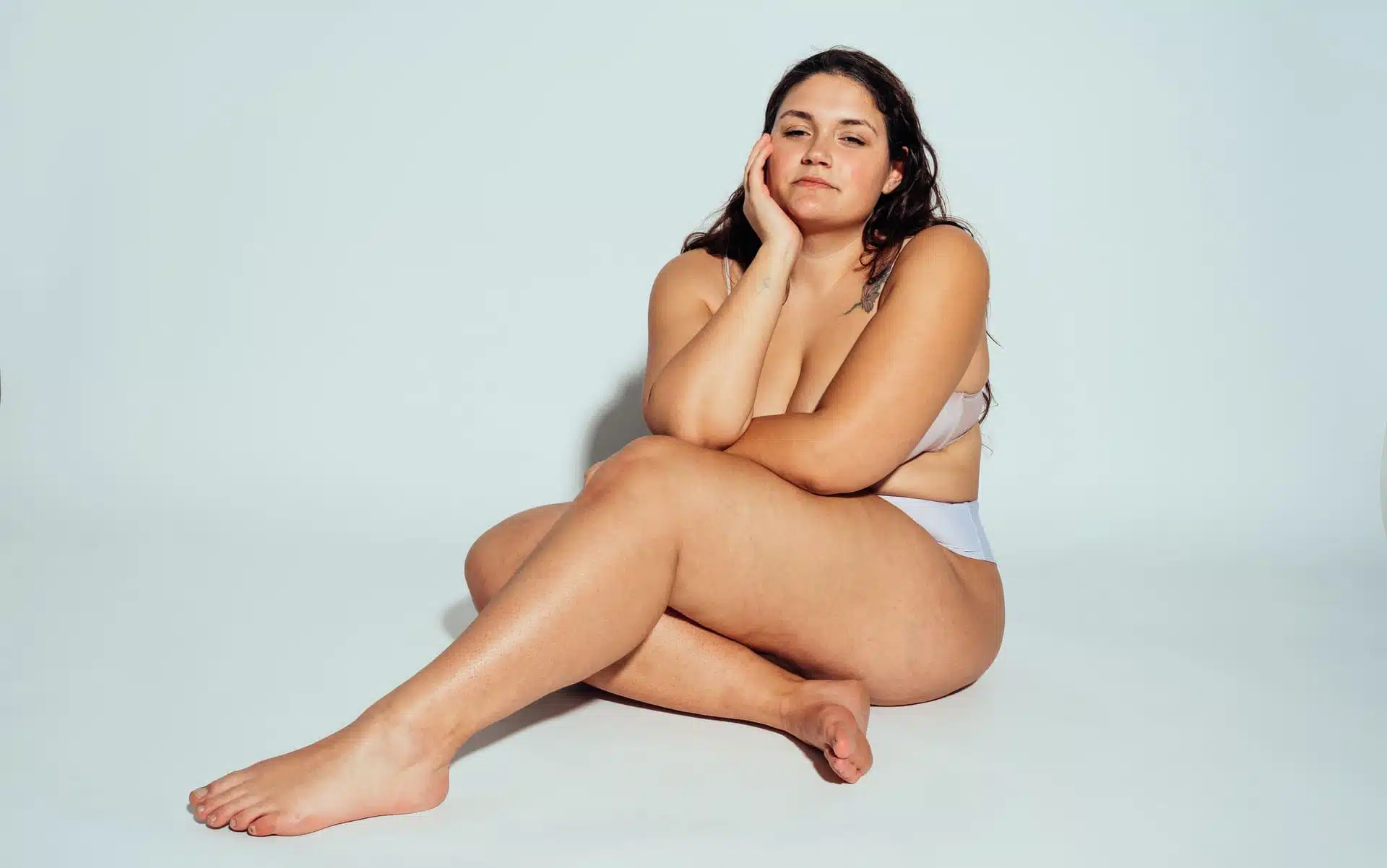 Woman in light lingerie sits with hand on chin against white background, symbolic image for Lipedema Symptoms at BONITAS in Nuremberg