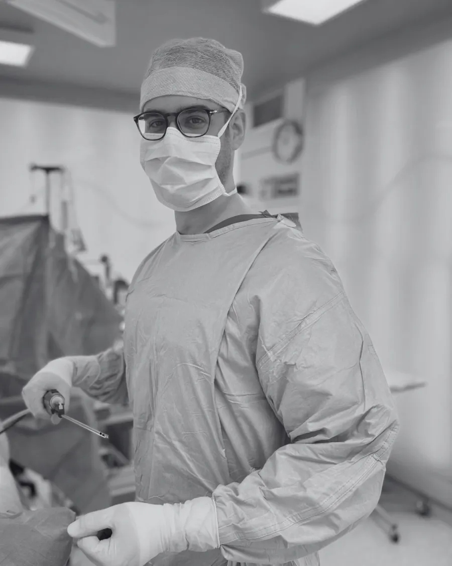 Schwarz-Weiß-Foto: Mann mit OP-Haube, Brille und Mundschutz hält eine Liposuktionskanüle im Operationssaal: Alejandro Marti, Facharzt für Plastische und Ästhetische Chirurgie, BONITAS Nürnberg