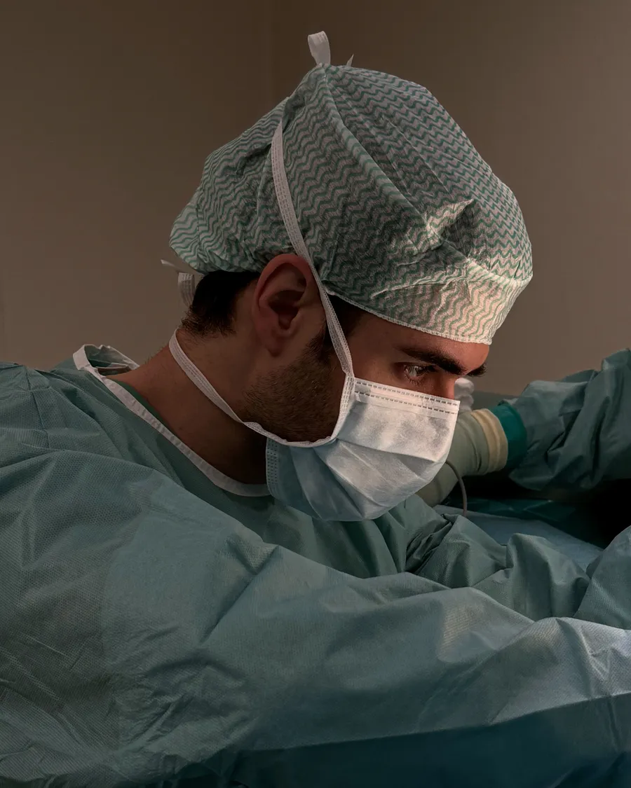Mann mit grün gemusterter OP-Haube und Mundschutz operiert konzentriert im Profil: Alejandro Marti, Facharzt für Plastische und Ästhetische Chirurgie, BONITAS Nürnberg