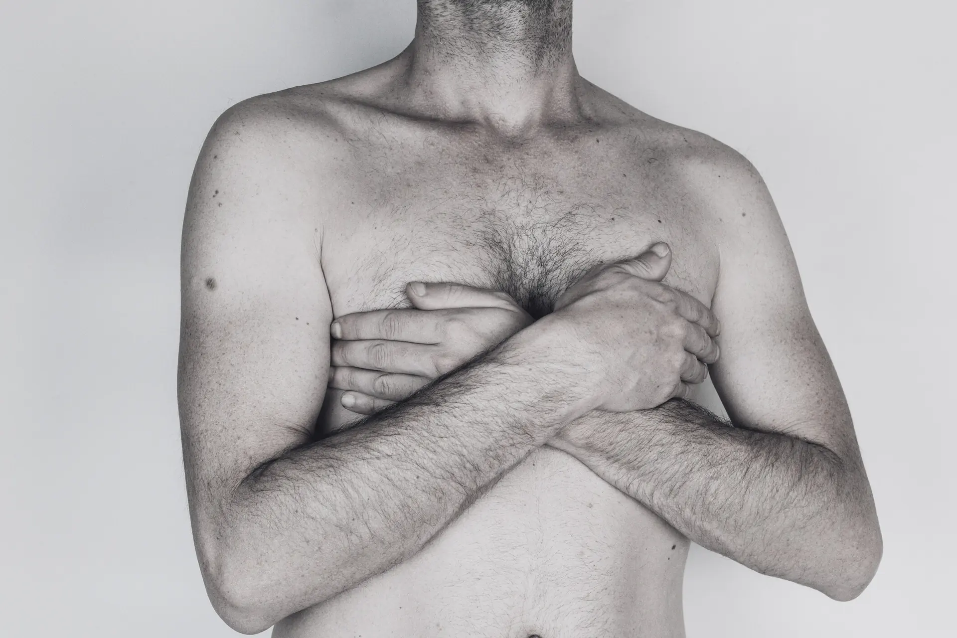 Shirtless man with his arms crossed over his chest against a light background, symbolic image on the subject of gynecomastia surgery at BONITAS in Nuremberg