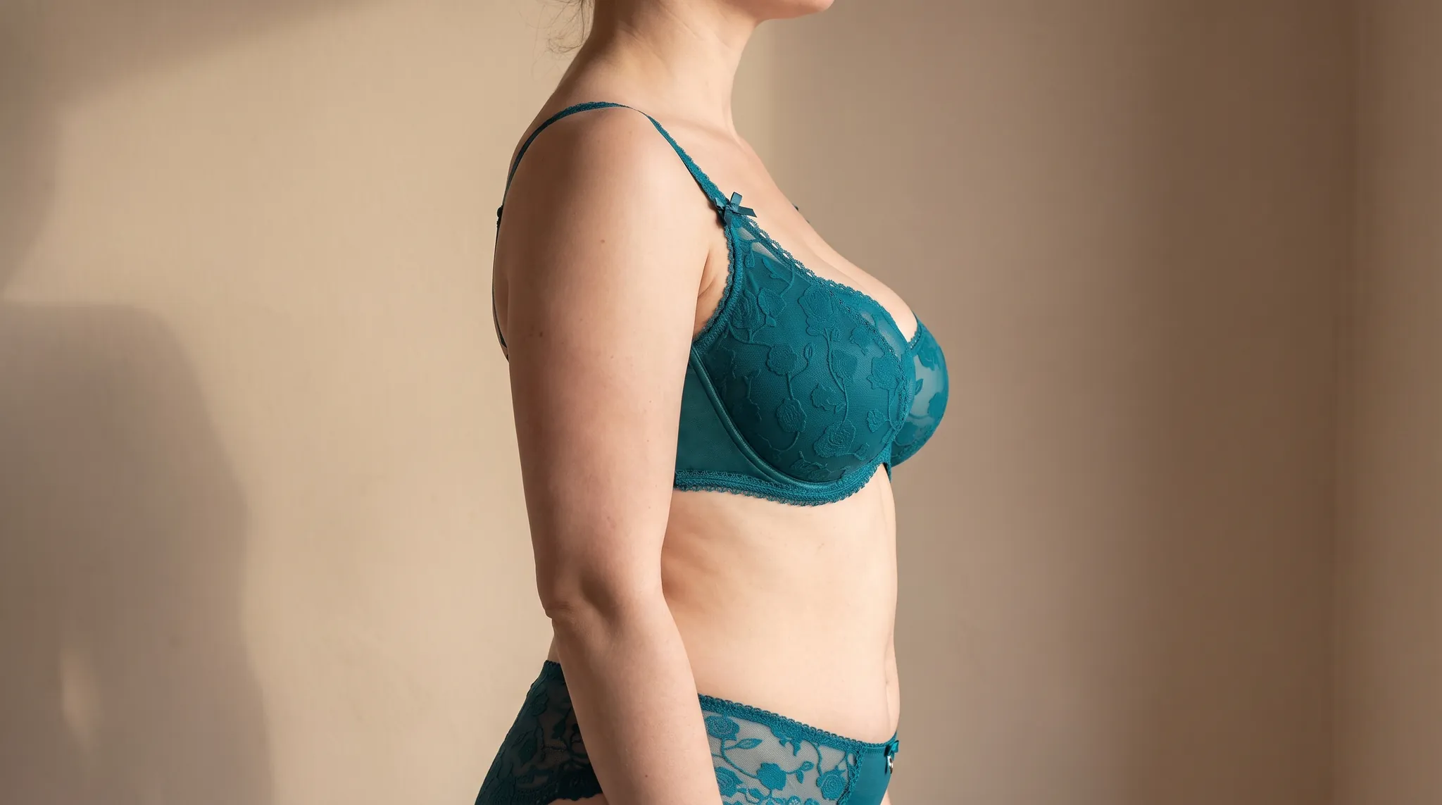 Upper body of a woman in profile, the forward projection of the breast clearly visible, in teal lace lingerie, symbolic image on the subject of implant profile and projection at BONITAS in Nuremberg