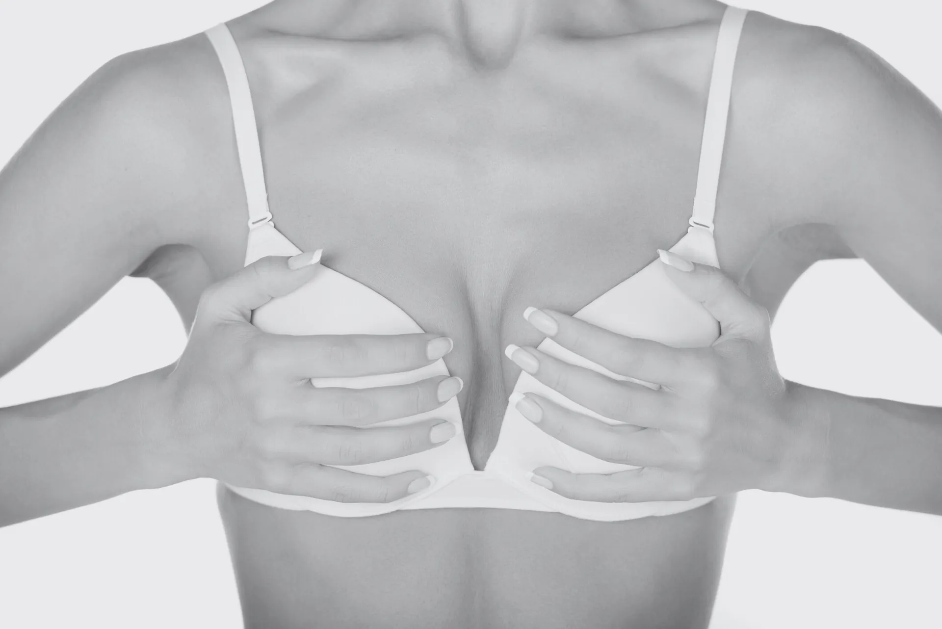 Woman in a white bra holding her breasts with both hands against a light background, symbolic image on the subject of cup size at BONITAS in Nuremberg