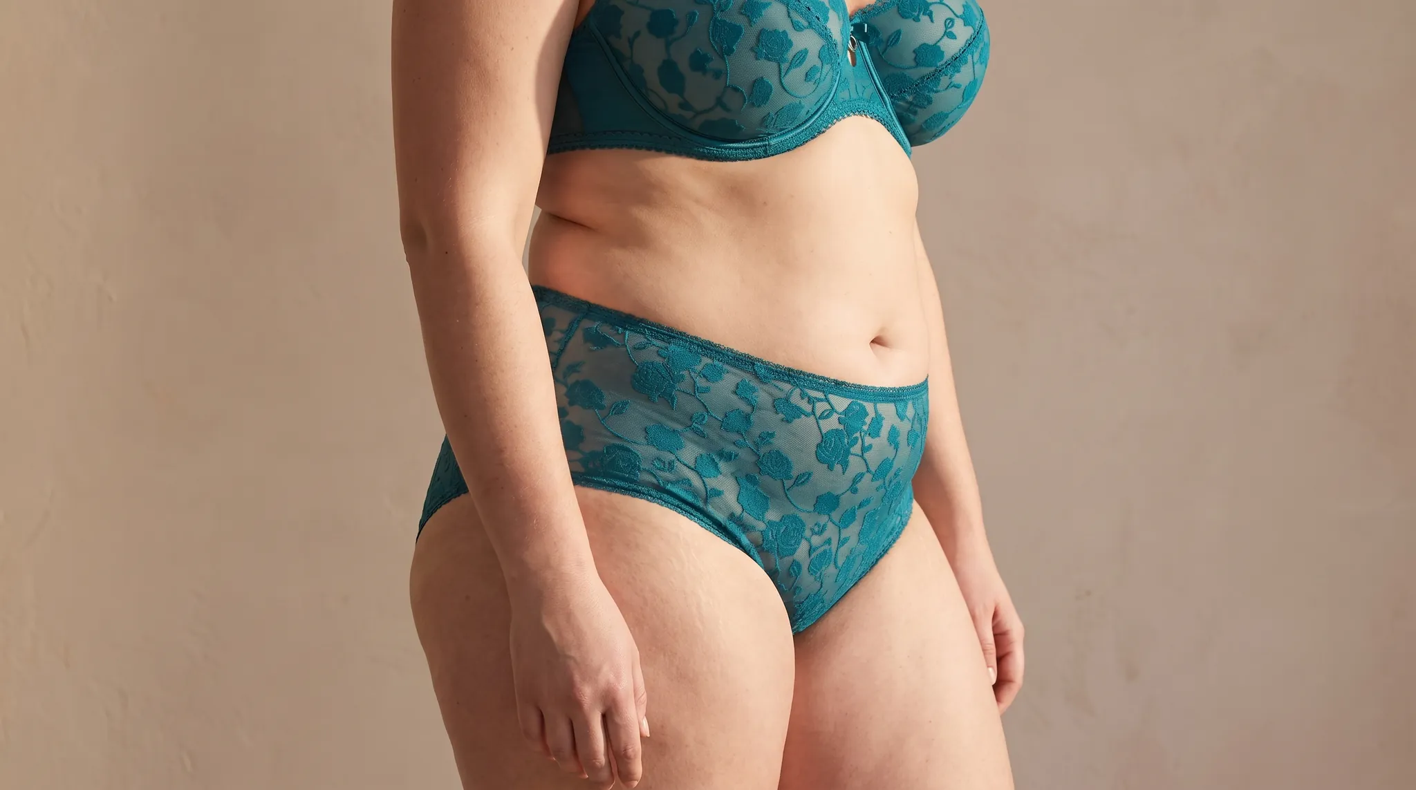 Abdomen and hips of a woman with a soft, rounded lower belly and full hips, in teal lace lingerie, symbolic image on the subject of lipedema on the abdomen at BONITAS in Nuremberg