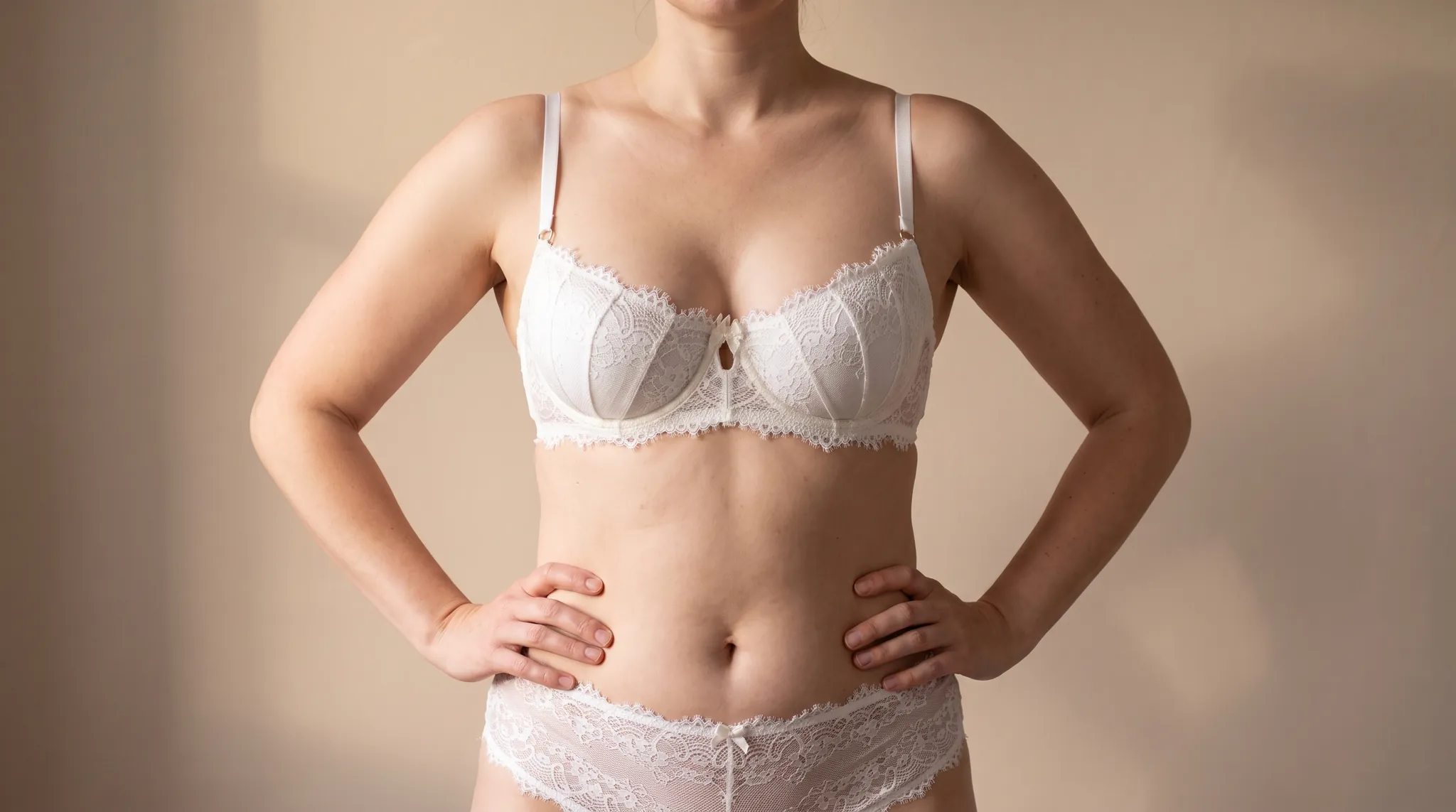 Oberkörper einer Frau mit harmonisch proportionierter Brust, die Hände an den Hüften, in cremefarbener Spitzenwäsche, Symbolbild zum Thema runde und anatomische Brustimplantate bei BONITAS in Nürnberg
