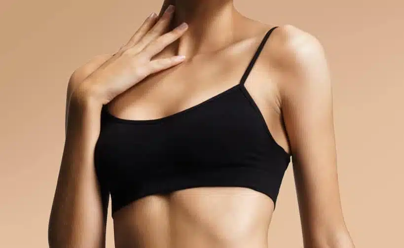 Mujer en top negro de tirantes con mano en el cuello fondo beige, imagen simbólica sobre Reducción de pecho en BONITAS Núremberg