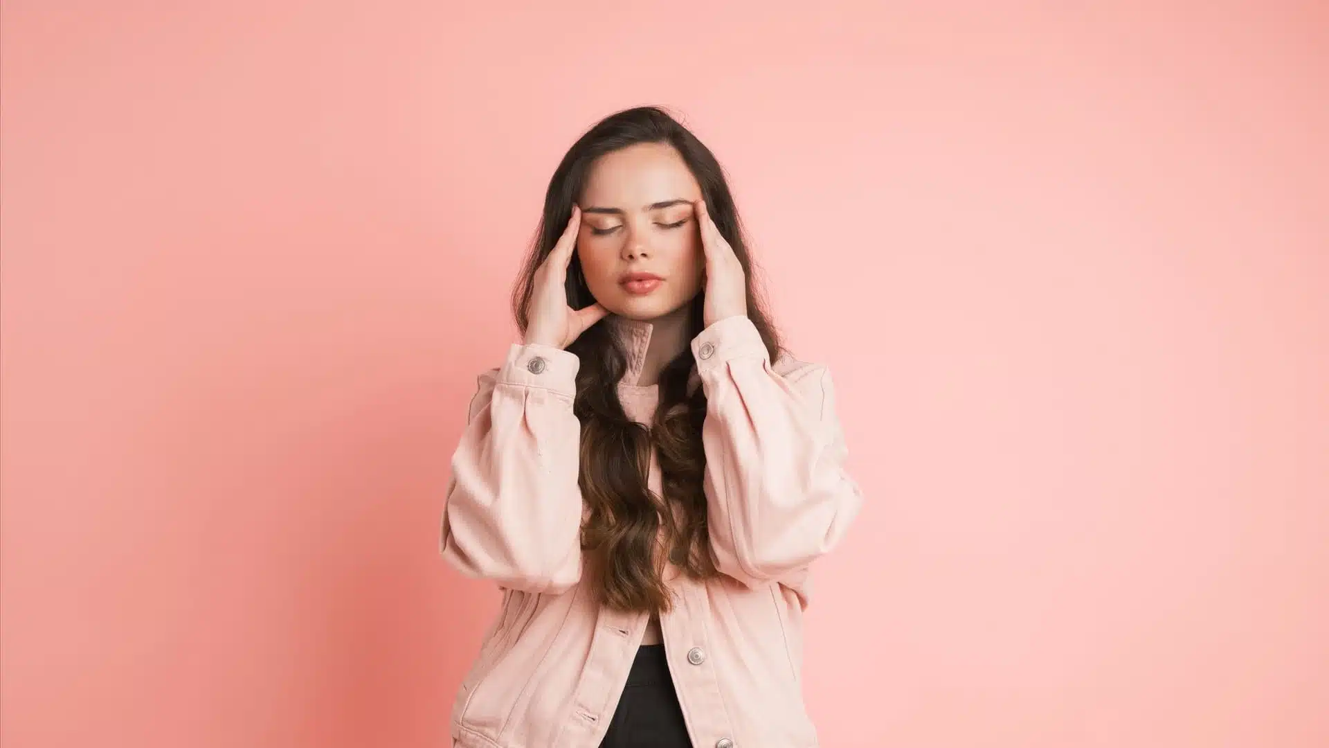 Mujer en chaqueta rosa se toca las sienes sobre fondo rosa, imagen simbólica sobre Tratamiento para la migraña en BONITAS Núremberg