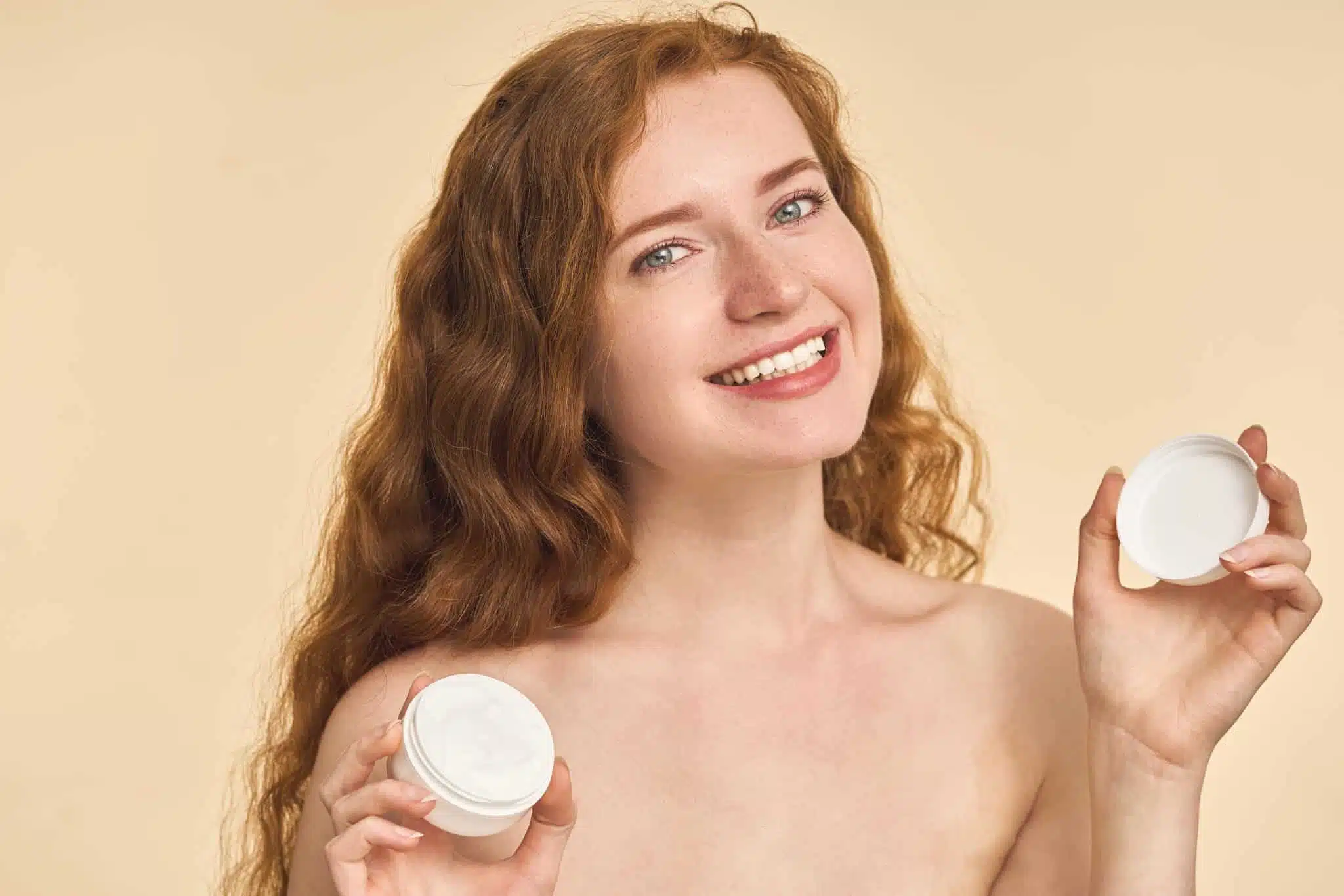Mujer sonriente de pelo rizado sostiene dos botes de crema fondo beige, imagen simbólica sobre Polinucleótidos en BONITAS Núremberg