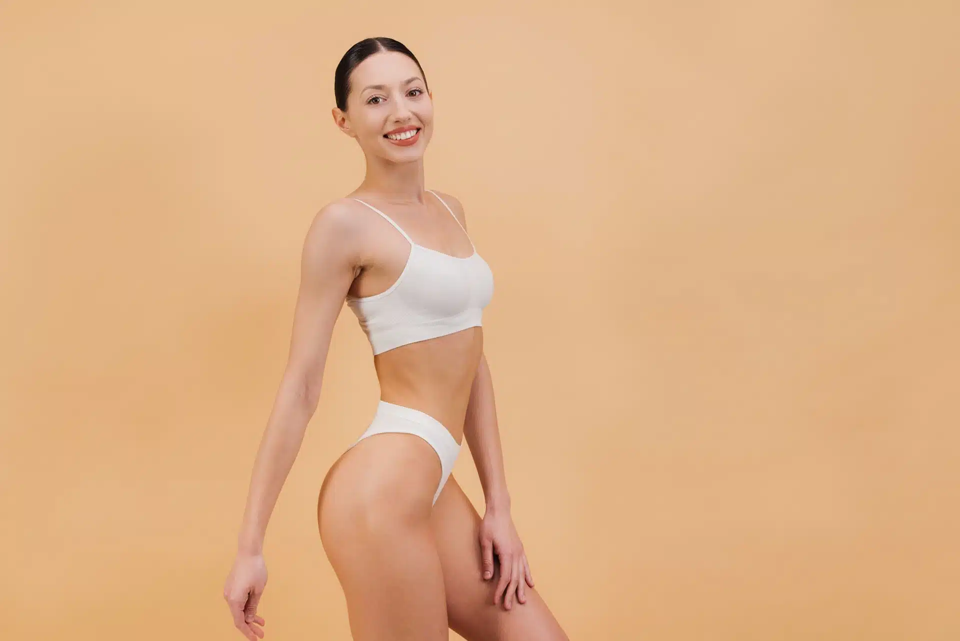 Smiling woman in white underwear standing against beige backdrop, symbolic image for Post-bariatric Surgery at BONITAS in Nuremberg