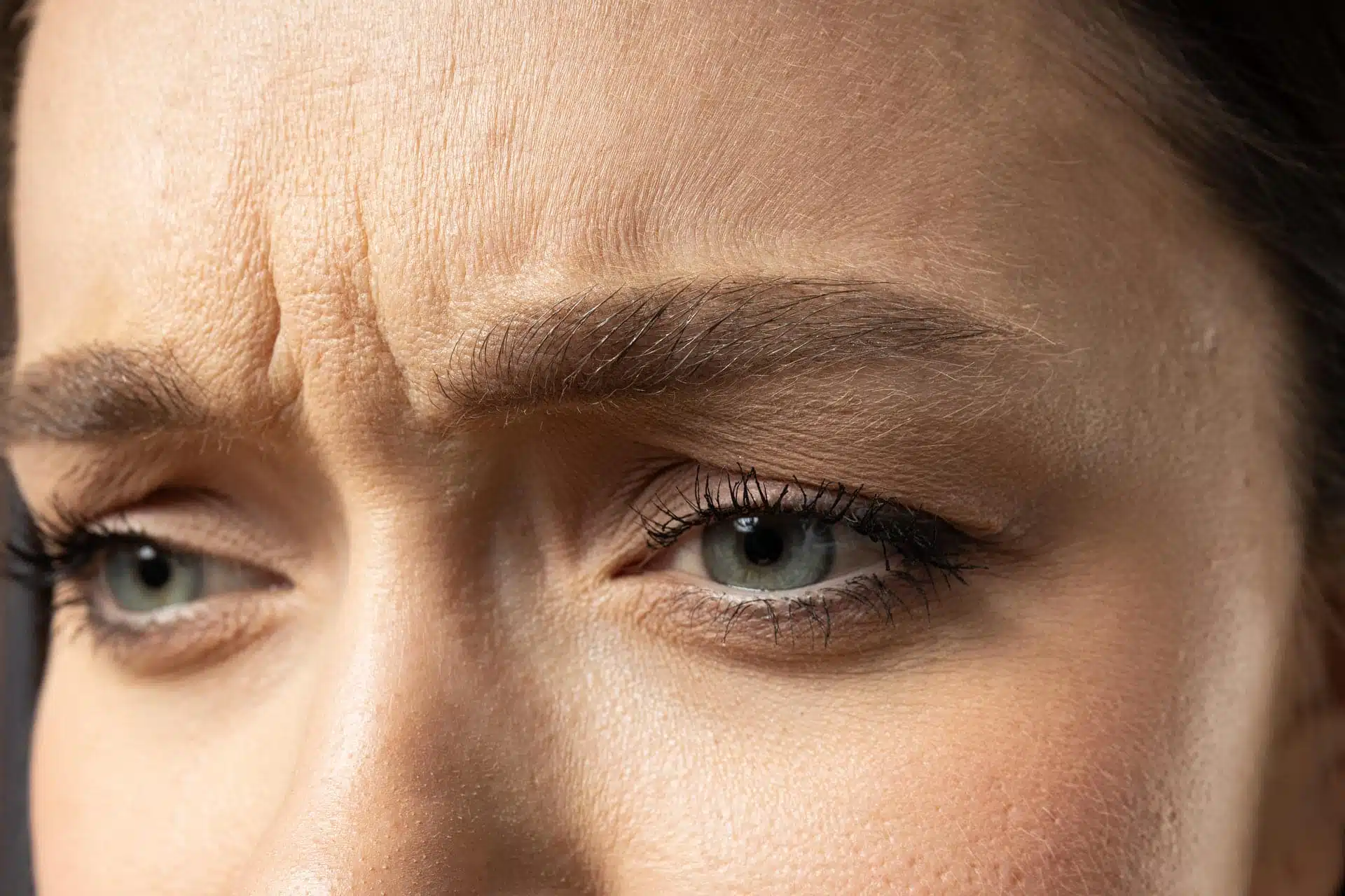 Mujer con ceño fruncido y mirada lateral sobre fondo oscuro, imagen simbólica sobre Eliminar el ceño fruncido en BONITAS Núremberg