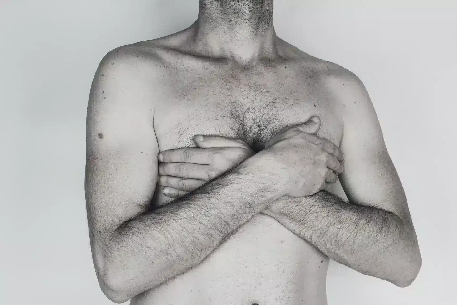 Shirtless man with his arms crossed over his chest against a light background, symbolic image on the subject of gynecomastia surgery at BONITAS in Nuremberg
