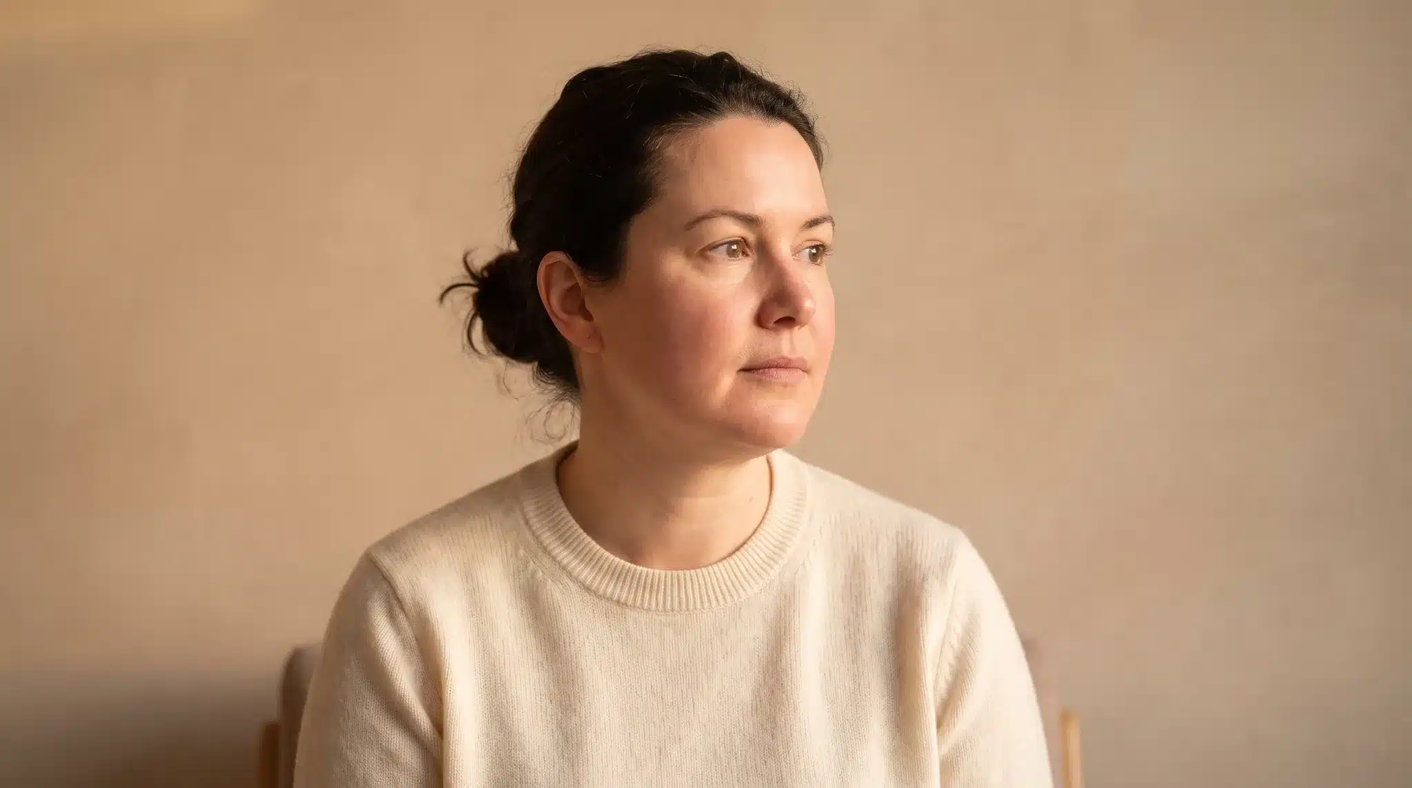 Gesicht einer Frau mit weichen, vollen Wangen und rundlicher Kieferlinie vor beiger Wand, Symbolbild zum Thema Lipödem im Gesicht bei BONITAS in Nürnberg